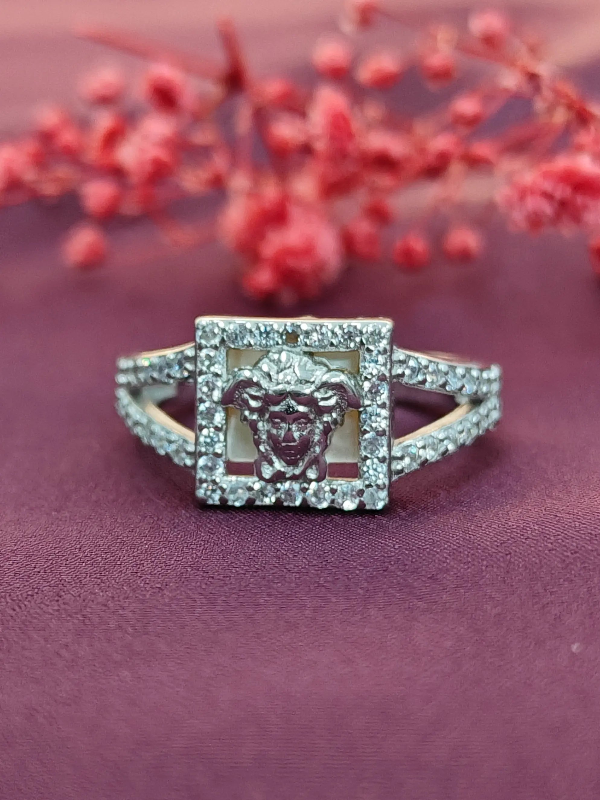 Silver ring with a lion emblem design on a purple surface with red flowers in the background